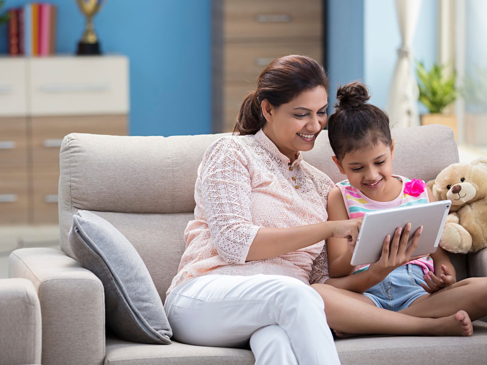 A young girl in primary school learning on a tablet with her mother at home