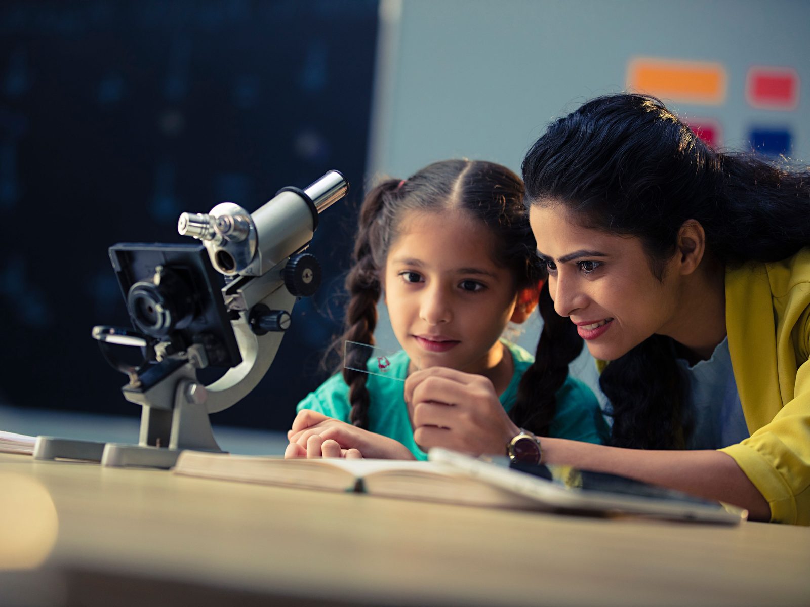 A middle-school student looking through a microscope with her teacher in science class