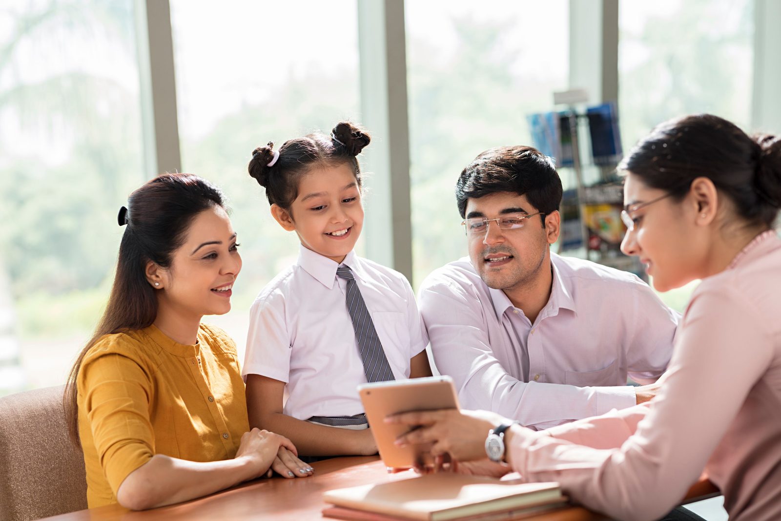 Parents and their daughter meeting a teacher at school, looking at a tablet together