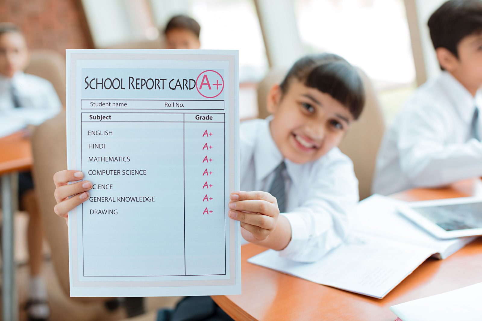 A student holding up a report card with A+ grades at the end of term