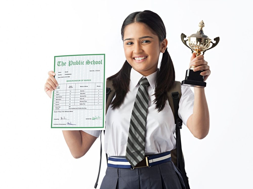 A student holding her marks sheet and a trophy