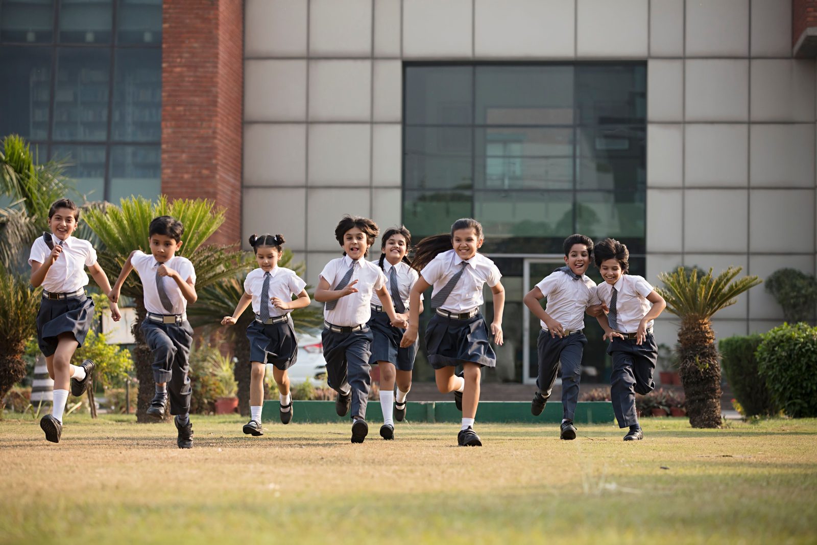 Children in school uniform running across the lawn of one school campus