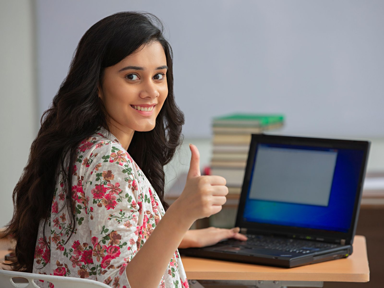 A smiling student giving a thumbs-up while revising a chapter on her laptop