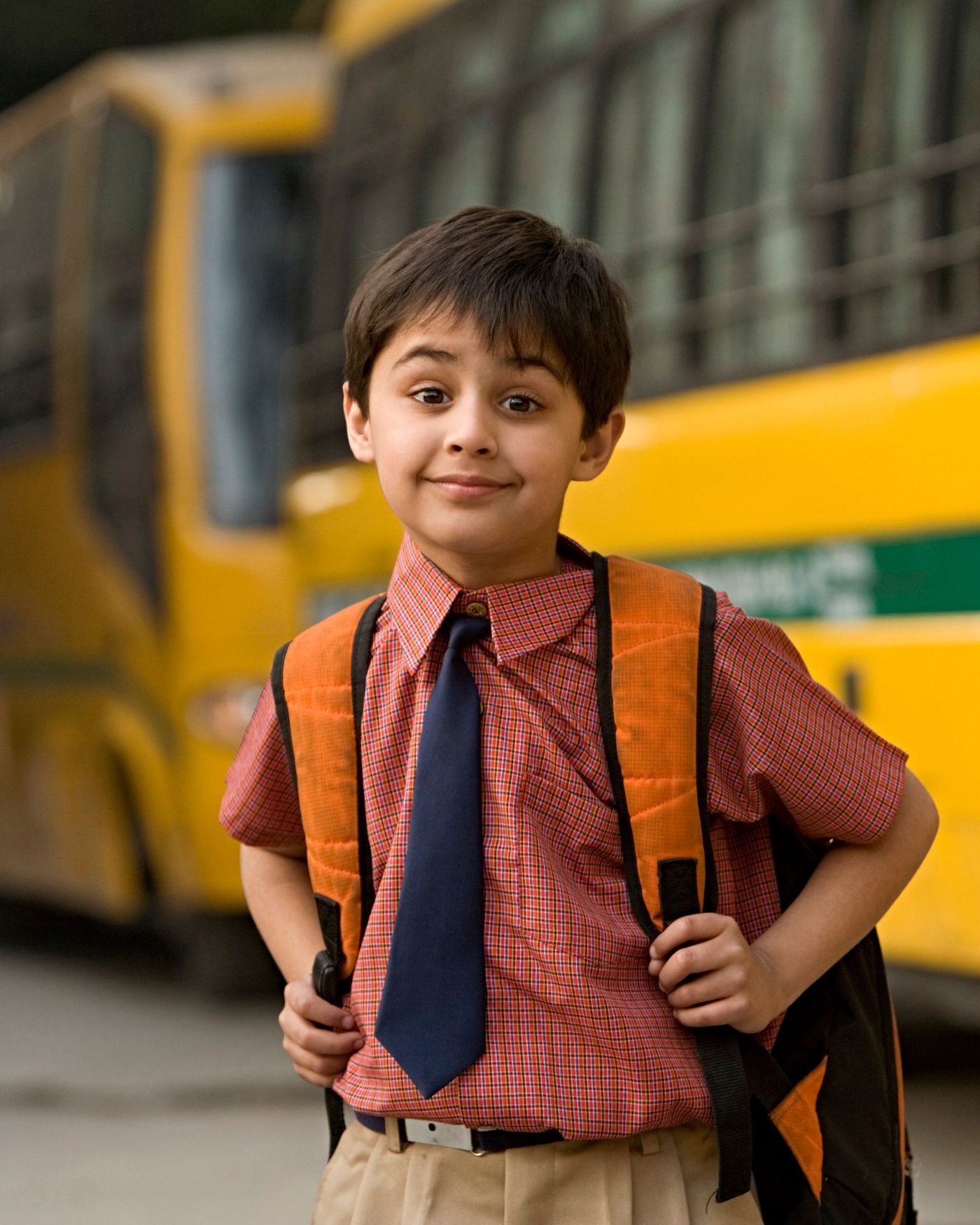 A schoolboy with his bag standing beside the yellow school bus he takes to school