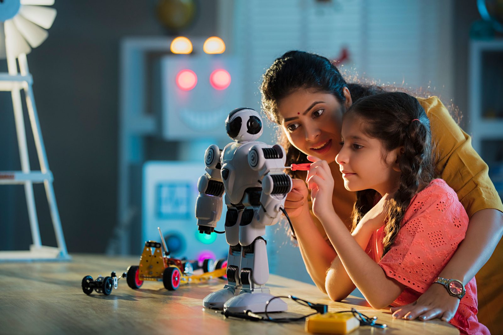 A teacher and a girl building a small robot together in a school robotics lab