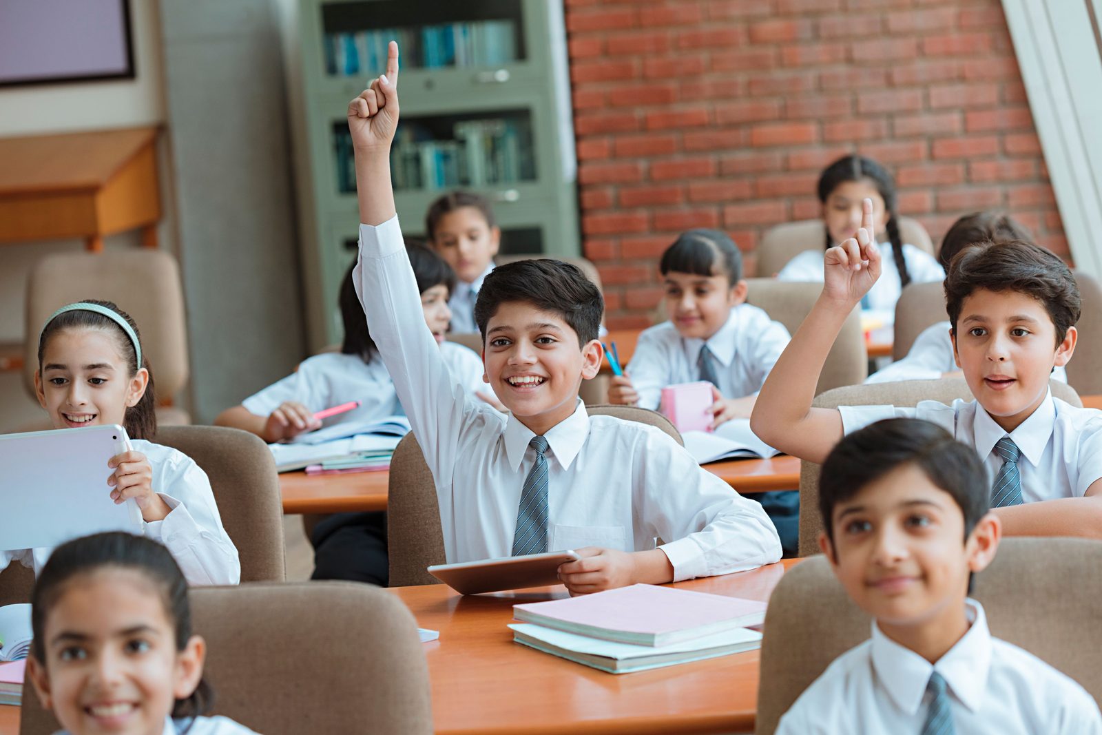 Students in a classroom raising their hands, present for the day