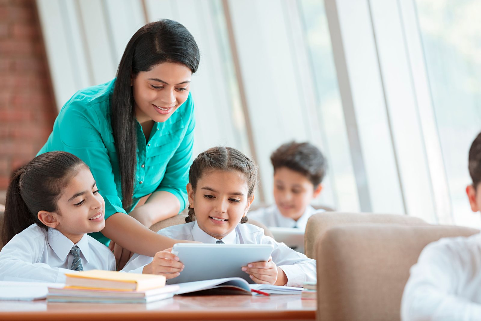 A teacher helping young students with tablets in class, where every child's data needs extra care